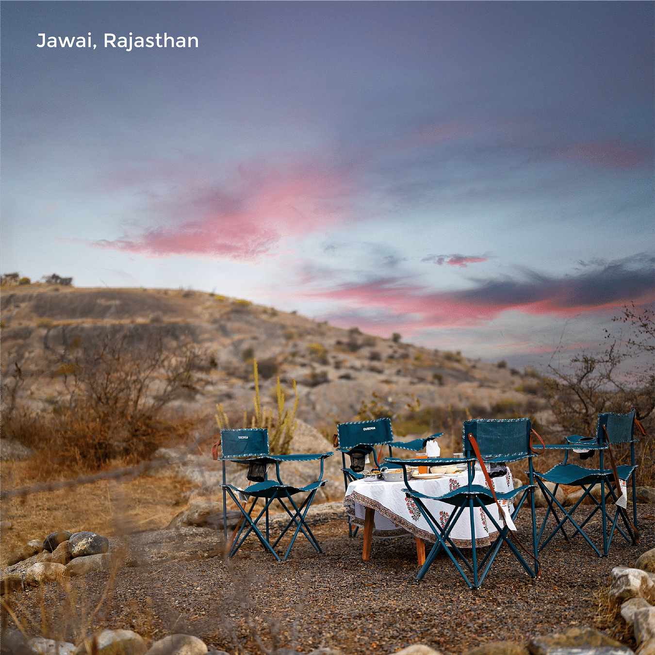 Image featuring an outdoor sitting area on the hill under a picturesque vibrant sky as the text says Jawai Rajasthan